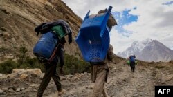 Sejumlah porter asal Pakistan mengangkut barang bawaan pendaki di jalur pendakian antara Askole dan K2, yang merupakan gunung tertinggi kedua di dunia, do Gilgit, Pakistan, pada 10 Juli 2023. (Foto: AFP/Joe Stenson)