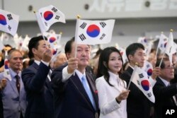 South Korean President Yoon Suk Yeol, center left, and and his wife, Kim Keon Hee, wave national flags during a ceremony to celebrate the anniversary of Korean Liberation Day from Japanese colonial rule in 1945, in Seoul, South Korea, Aug. 15, 2023.