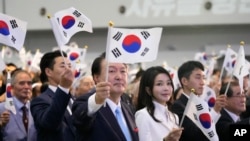South Korean President Yoon Suk Yeol, center left, and and his wife, Kim Keon Hee, wave national flags during a ceremony to celebrate the anniversary of Korean Liberation Day from Japanese colonial rule in 1945, in Seoul, South Korea, Aug. 15, 2023.