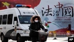 资料照：一辆警车和一名女子骑车驶过北京街头一堵宣传中国法治的宣传墙。（2016年12月28日）