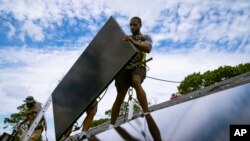 FILE - Employees of NY State Solar, a residential and commercial photovoltaic systems company, install solar panels on a roof, Aug. 11, 2022, in Massapequa, NY.