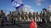Seorang demonstran duduk di jalan raya sambil membawa bendera Israel, di kelilingi polisi perbatasan paramiliter dalam aksi protes terhadap rencana pemerintah PM Benjamin Netanyahu untuk merombak sistem peradilan, di Tel Aviv, Israel, Kamis, 9 Maret 2023. (AP/ Ariel Schalit)