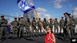 Seorang demonstran duduk di jalan raya sambil membawa bendera Israel, di kelilingi polisi perbatasan paramiliter dalam aksi protes terhadap rencana pemerintah PM Benjamin Netanyahu untuk merombak sistem peradilan, di Tel Aviv, Israel, Kamis, 9 Maret 2023. (AP/ Ariel Schalit)