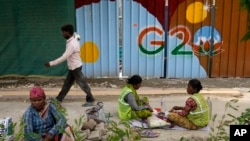 Laborers take a lunch break near a construction site covered with G20 summit logo in New Delhi, India, Thursday, Aug. 24, 2023. (AP Photo/Manish Swarup)