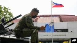 FILE - A soldier uses his smartphone on top of an armored personnel carrier in Quezon City, Philippines, on May 23, 2022. 