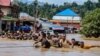 Orang-orang memegang tali berjalan melewati banjir setelah Sungai Kobe meluap akibat hujan lebat di Lukulamo, Maluku Utara hari Senin (22/7). (Foto:&nbsp;&nbsp;Azzam Risqullah / AFP)