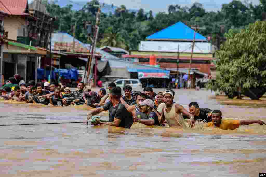 Orang-orang memegang tali berjalan melewati banjir setelah Sungai Kobe meluap akibat hujan lebat di Lukulamo, Maluku Utara hari Senin (22/7). (Foto:&nbsp;&nbsp;Azzam Risqullah / AFP)