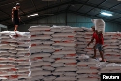 Seorang pekerja berdiri di atas tumpukan karung beras sementara pekerja lainnya membawa karung beras di gudang di Jakarta, Indonesia, 13 Februari 2024. (REUTERS/Ajeng Dinar Ulfiana)