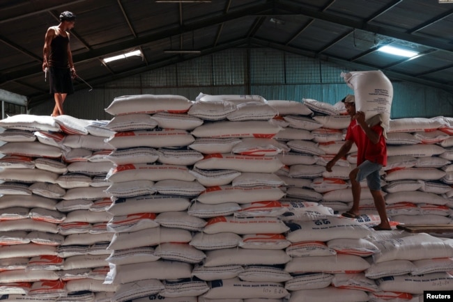 Seorang pekerja berdiri di atas tumpukan karung beras sementara pekerja lainnya membawa karung beras di gudang di Jakarta, Indonesia, 13 Februari 2024. (REUTERS/Ajeng Dinar Ulfiana)