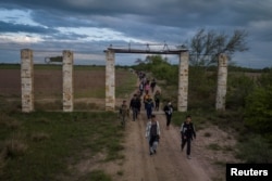 FILE - Migrants from Central America and China are escorted by members of the Texas Army National Guard as they walk to a staging point past farmland after crossing the Rio Grande river into the U.S. from Mexico in Fronton, Texas, April 10, 2023.