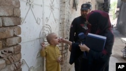 FILE - A police officer stands guard as a health worker administers a polio vaccine to a child at a neighborhood of Peshawar, Pakistan, May 22, 2023. 
