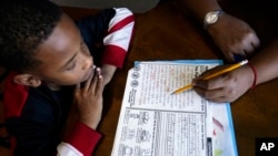 Christian Ensrud, 7, watches as his mother, Tamela Ensrud, help him with his homework at their home Monday, Nov. 21, 2022, in Nashville, Tenn. (AP Photo/Mark Humphrey)