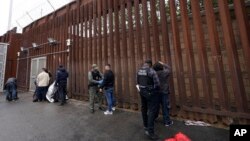 ARCHIVO: Agentes federales quitan las esposas a migrantes liberados hacia Tijuana, México, frente a una puerta del muro fronterizo en San Diego, California, el 15 de marzo de 2023.