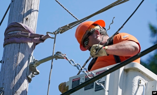 FILE - Travis Sheetz, a worker with the Mason County (Wash.) Public Utility District, installs fiber optic cable on a utility pole, Aug. 4, 2021, near Belfair, Washington.