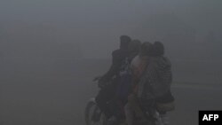 People on a motor bike make their way along a street amid heavy smog in Lahore, Pakistan.