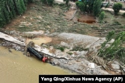 In this photo released by Xinhua News Agency, a drone photo taken on Aug. 21, 2024, shows a vehicle overturned by floodwaters in Heishanke Township, the city of Huludao in Liaoning province.