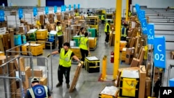 FILE - Amazon employees load packages onto carts before they are transferred to trucks for distribution, at an Amazon facility in South Gate, California, July 16, 2024.