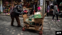 FILE - An elderly woman pushes a cart after searching through rubbish bins to collect recyclable items to sell, along a street near the Great Hall of the People in Beijing on March 5, 2021.