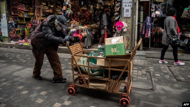 FILE - An elderly woman pushes a cart after searching through rubbish bins to collect recyclable items to sell, along a street near the Great Hall of the People in Beijing on March 5, 2021.