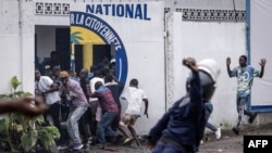 FILE - A Police officer throws a rock as opposition supporters run into a opposition leader Martin Fayulu's party house during a demonstration in Kinshasa, Democratic Republic of Congo, Dec. 27, 2023.