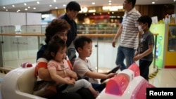 A person holds a girl as a boy drives a toy car at a shopping mall in Shanghai, China June 1, 2021. (REUTERS/Aly Song)