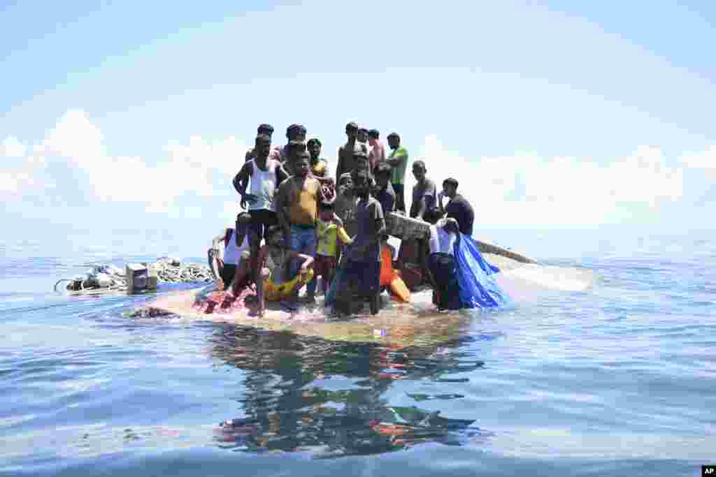Rohingya refugees stand on their capsized boat before being rescued in the waters off West Aceh, Indonesia. (AP Photo/Reza Saifullah)