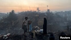 A Rohingya refugee family stands near their shelter that has been destroyed after a fire broke out in the Rohingya refugee camp in Balukhali in Cox's Bazar, Bangladesh, March 5, 2023. 