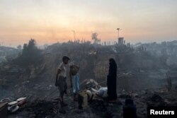 Keluarga pengungsi Rohingya berdiri di dekat tempat penampungan mereka yang telah hancur setelah kebakaran terjadi di kamp pengungsi Rohingya di Balukhali di Cox's Bazar, Bangladesh, 5 Maret 2023. (Foto: REUTERS/Ro Yassin Abdumonab)