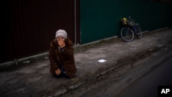 A woman kneels as the funeral procession with the body of Kostiantyn Kostiuk passes by during his funeral in Borova, near Kyiv, Ukraine, Feb. 18, 2023