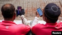 Para pengemudi layanan pengantaran makanan online tampak memeriksa telepon genggam mereka, saat menunggu pesanan dari pelanggan di luar gedung perkantoran di Karachi, Pakistan, pada 22 Agustus 2024. (Foto: Reuters/Akhtar Soomro)