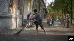 Local residents clean the street from broken glass that fell down from the windows of their apartments and shops after Russian rocket attack in Kyiv, Ukraine, Aug. 30, 2023.
