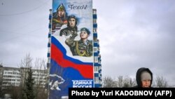 FILE - A pedestrian walks by an office of the ruling United Russia Party, with its emblem bear and a patriotic mural on the wall in the town of Chekhov, 75 kilometers from Moscow, Feb. 11, 2023.