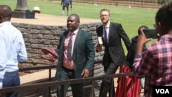 Tapiwa Muchineripi (holding shoes) and Douglas Coltart (holding book) of Zimbabwe Lawyers for Human Rights arrive at Harare Magistrates Court on Sept. 5, 2023, to face charges of obstructing or defeating the course of justice. (Columbus Mavhunga/VOA)