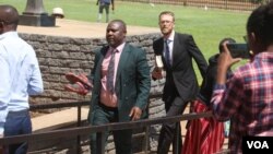 Tapiwa Muchineripi (holding shoes) and Douglas Coltart (holding book) of Zimbabwe Lawyers for Human Rights arrive at Harare Magistrates Court on Sept. 5, 2023, to face charges of obstructing or defeating the course of justice. (Columbus Mavhunga/VOA)