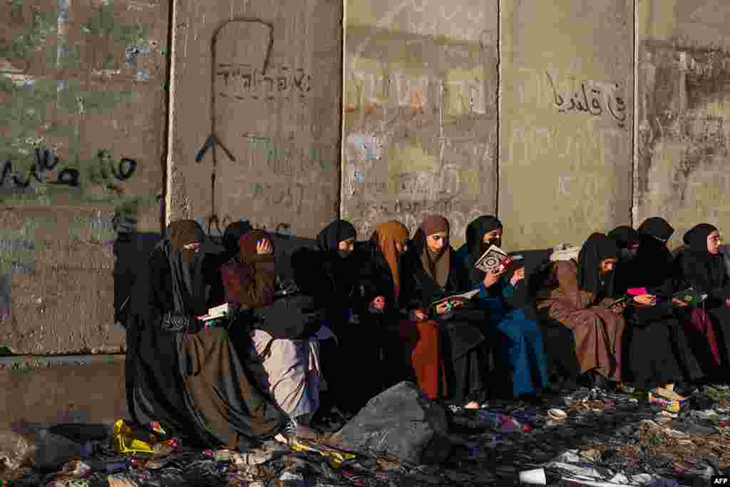 Palestinian women read the Koran as they wait in front of a concrete barrier at a checkpoint in Qalandia, in the occupied West Bank, to cross into Jerusalem for the first Friday noon prayer of the Muslim holy fasting month of Ramadan at the Al-Aqsa Mosque.