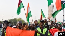 FILE - Supporters of the Alliance Of Sahel States hold up flags as they celebrate Mali, Burkina Faso and Niger leaving the Economic Community of West African States (ECOWAS) in Niamey, Jan. 28, 2024.