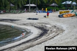 Seorang pekerja membersihkan tumpahan minyak dalam kantong plastik di Pantai Siloso di Pulau Sentosa di Singapura, 15 Juni 2024. Pantai itu ditutup karena tumpahan minyak di pelabuhan terdekat. (Foto: Roslan Rahman/AFP)