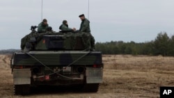 FILE - Ukrainian and Polish soldiers sit on top of a German-made Leopard 2 tank during training at a military base and test range in Swietoszow, Poland, Feb. 13, 2023.