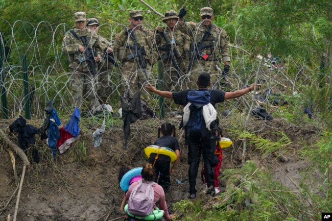 A migrant gestures to Texas National Guards standing behind razor wire on the bank of the Rio Grande river, seen from Matamoros, Mexico, Thursday, May 11, 2023. Pandemic-related U.S. asylum restrictions, known as Title 42, are to expire May 11. (AP Photo/Fernando Llano)