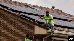 FILE - Workers install solar panels on the roof of a house in Rivas Vaciamadrid, Spain, Sept. 15, 2022. 