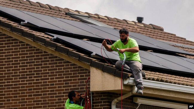 FILE - Workers install solar panels on the roof of a house in Rivas Vaciamadrid, Spain, Sept. 15, 2022.