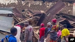 People stand next to a building that collapsed in torrential rains, in western Rwanda, May 3, 2023.