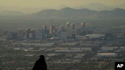 FILE - A man overlooks downtown Phoenix at sunset atop South Mountain, Sunday, July 30, 2023. Phoenix hit its 31st consecutive day of at least 110 degrees Fahrenheit (43.3 Celsius). 