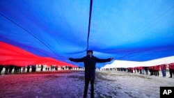 A Navy school cadet stands under a giant Russian flag during an action to mark the ninth anniversary of when Russia annexed Crimea from Ukraine, in St. Petersburg, Russia, March 18, 2023. The annexation has been denounced by most world leaders.