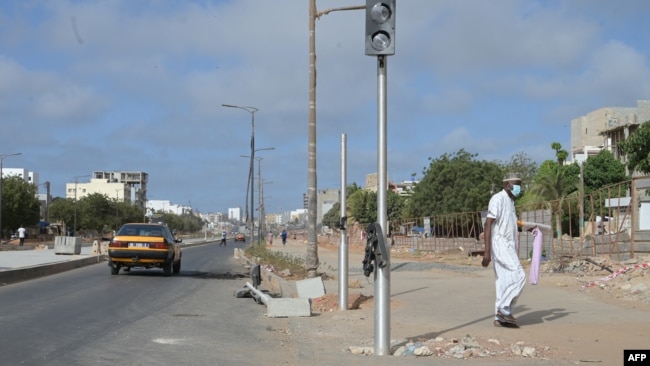 Un piéton passe devant un feu de signalisation brisé dans une rue de Dakar le 3 juin 2023, suite aux violences meurtrières dans la capitale sénégalaise (Photo by Seyllou / AFP)