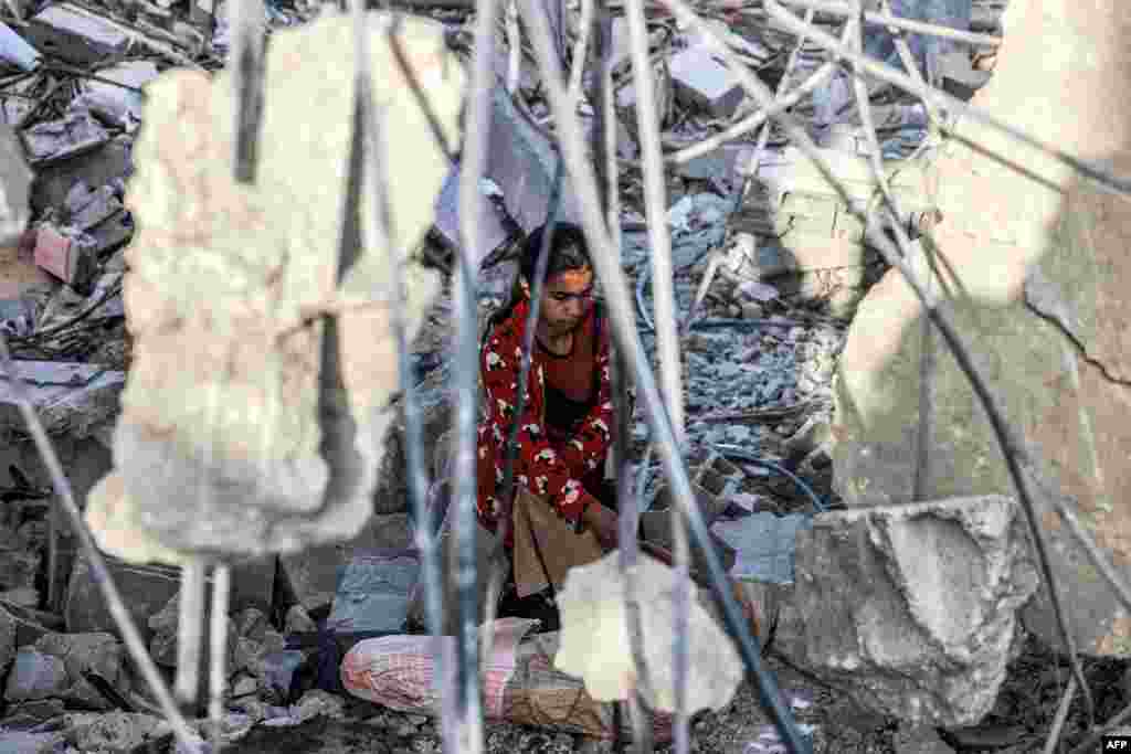 Seorang gadis berusaha menyelamatkan barang-barang dari puing-puing bangunan yang runtuh di kota Rafah, Jalur Gaza selatan, pascaserangan udara Israel Selasa malam. (AFP)&nbsp;