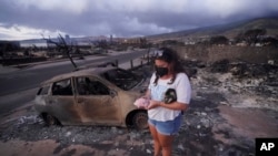 Summer Gerling picks up her piggy bank, found in the rubble of her home following the wildfire Aug. 10, 2023, in Lahaina, Hawaii.