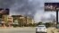 Smoke rises in the background as a car drives along an almost deserted street in Khartoum on April 16, 2023, during ongoing fighting between the forces of two rival generals. 
