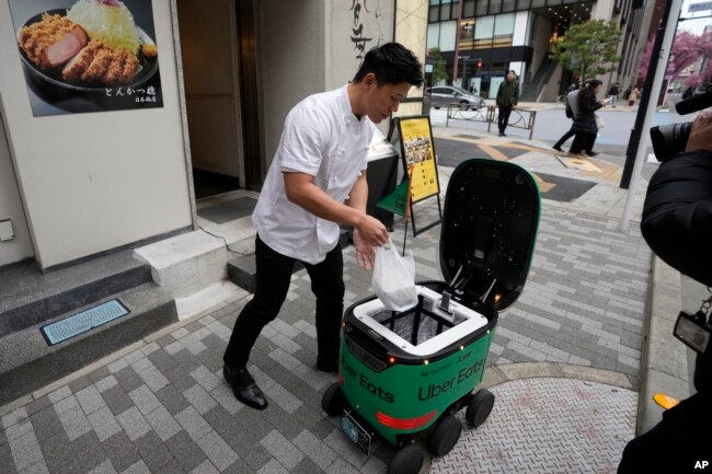 Seorang pekerja restoran meletakkan makanan pesanan dalam wadah robot pengantar makanan Uber Eats saat demonstrasi untuk media di Tokyo, Jepang, Selasa, 5 Maret 2024. (AP/Shuji Kajiyama)