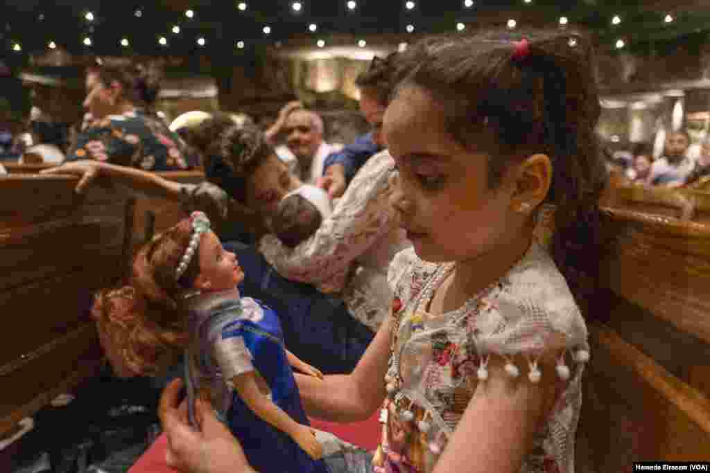 Sara, an 8-year-old schoolgirl, sits with her parents and siblings on a long pew inside the Virgin Mary Monastery. She dressed up her Barbie doll in a Mary-inspired costume for the celebrations.